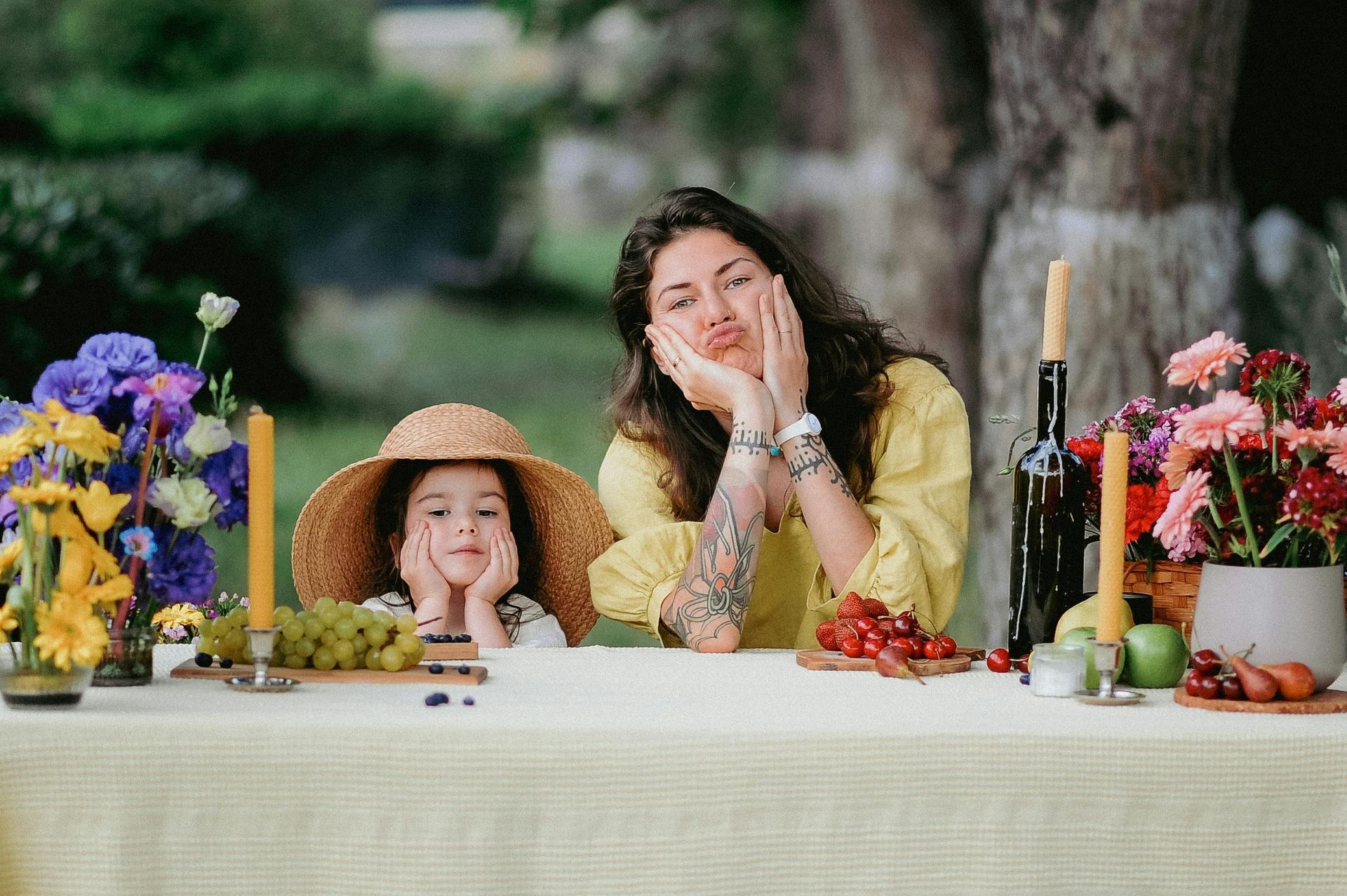 Vrouw en kind aan een picknicktafel, beiden trekken een gek gezicht. Bloemen en eten sieren de tafel.