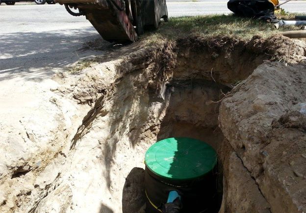 A man is kneeling in a hole in the ground next to a truck.