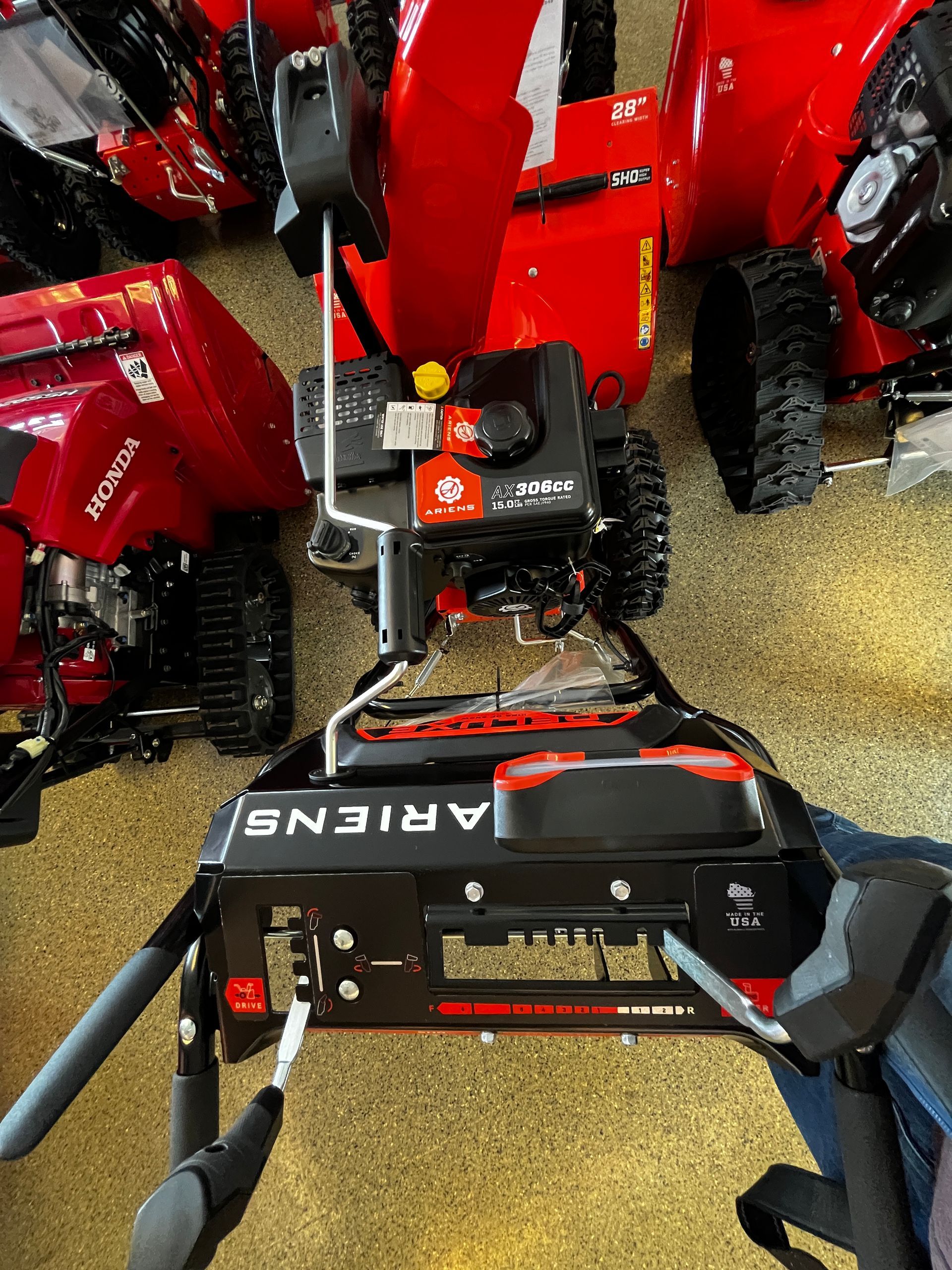 A red snow blower is sitting in a garage next to other snow blowers.