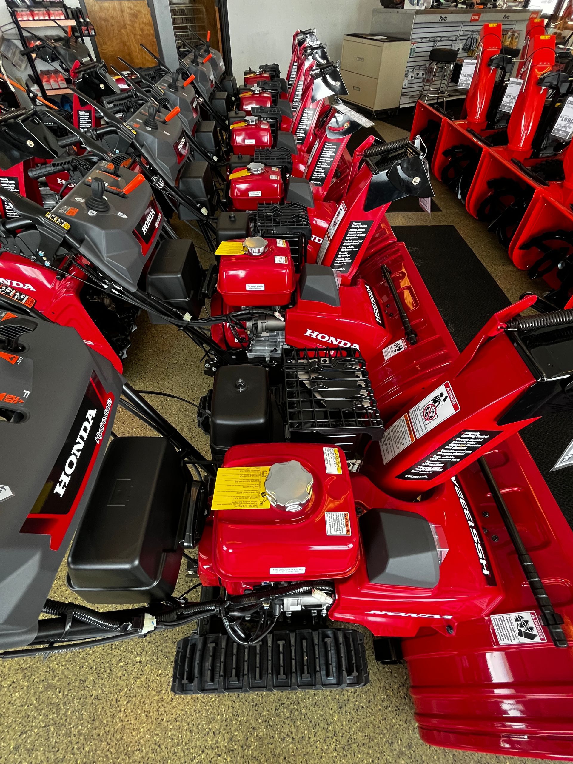 A row of red snow blowers are lined up in a showroom.
