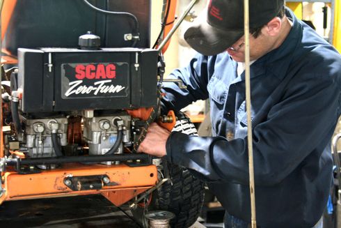 A man is working on a scag zero turn tractor
