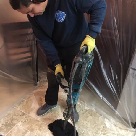 Ted & Bros Plumbing | man wearing yellow gloves is using a drill on a tiled floor.