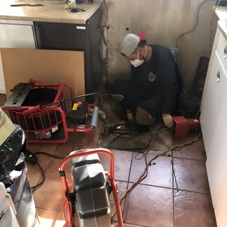 Ted & Bros Plumbing | man wearing a mask is working on a drain in a kitchen.