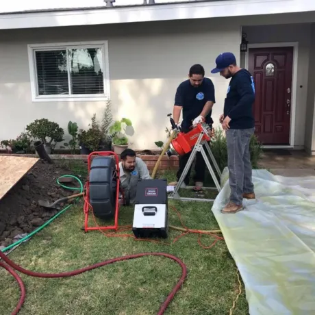 Ted & Bros Plumbing | group of men are working on a drain in front of a house.