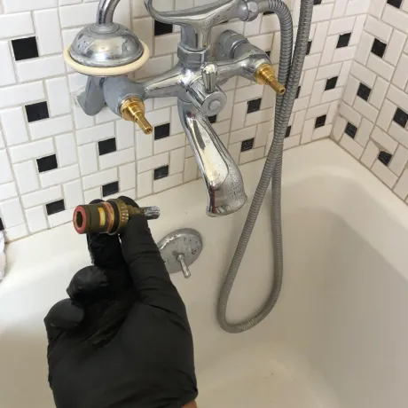 Ted & Bros Plumbing | person wearing black gloves is holding a faucet in front of a bathtub.