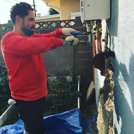 Ted & Bros Plumbing | man in a red shirt is working on a pipe