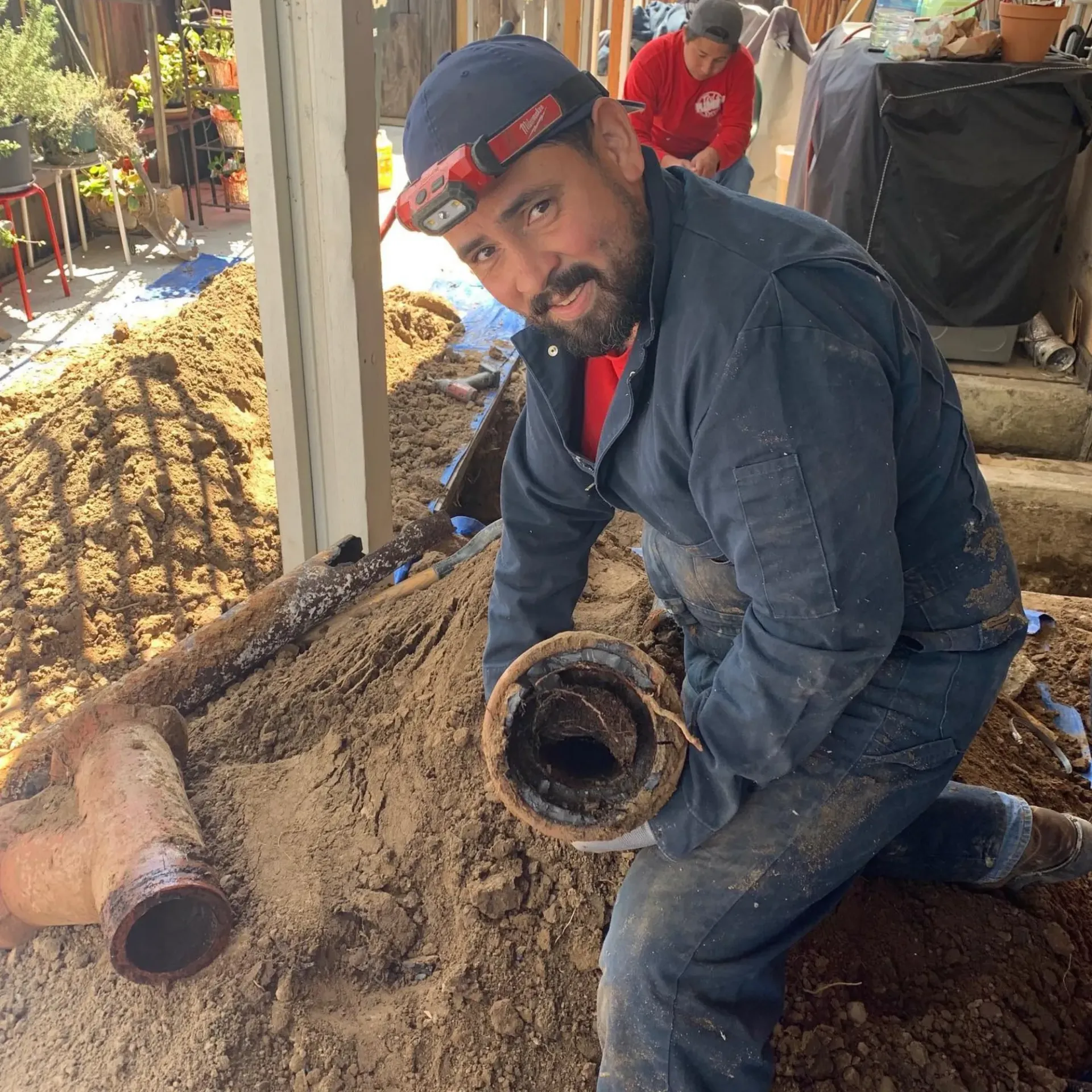 Ted & Bros Plumbing | man is kneeling down in the dirt holding a pipe