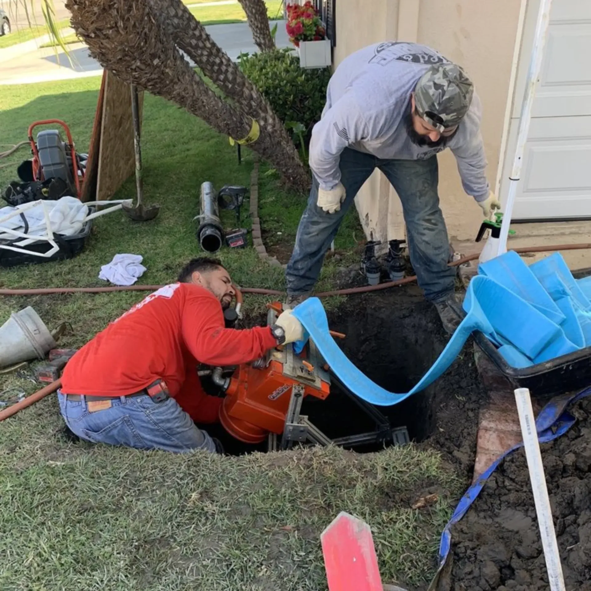 Ted & Bros Plumbing | Two men are working on a drain in a yard.