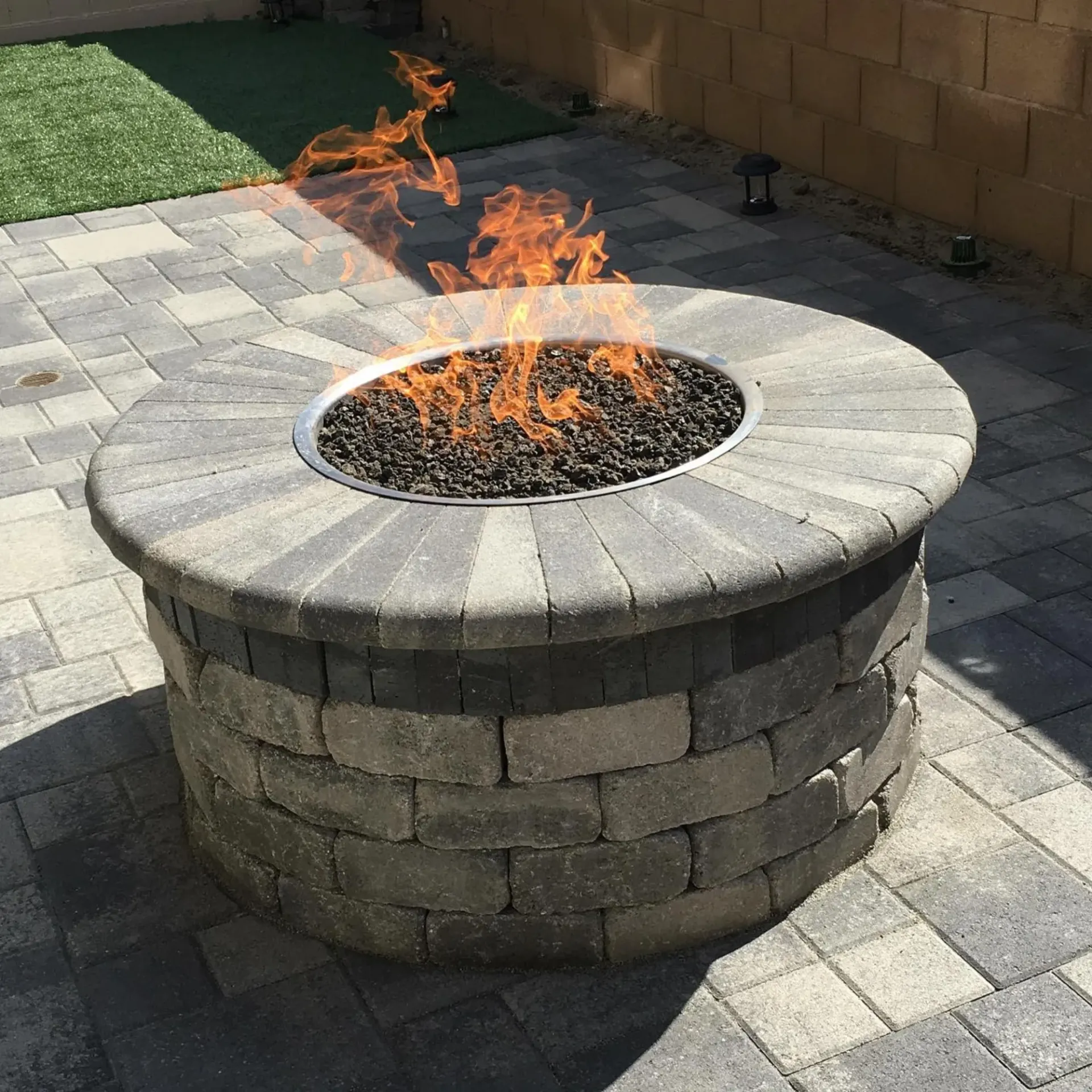 Ted & Bros Plumbing | fire pit is sitting on a brick patio with flames coming out of it.