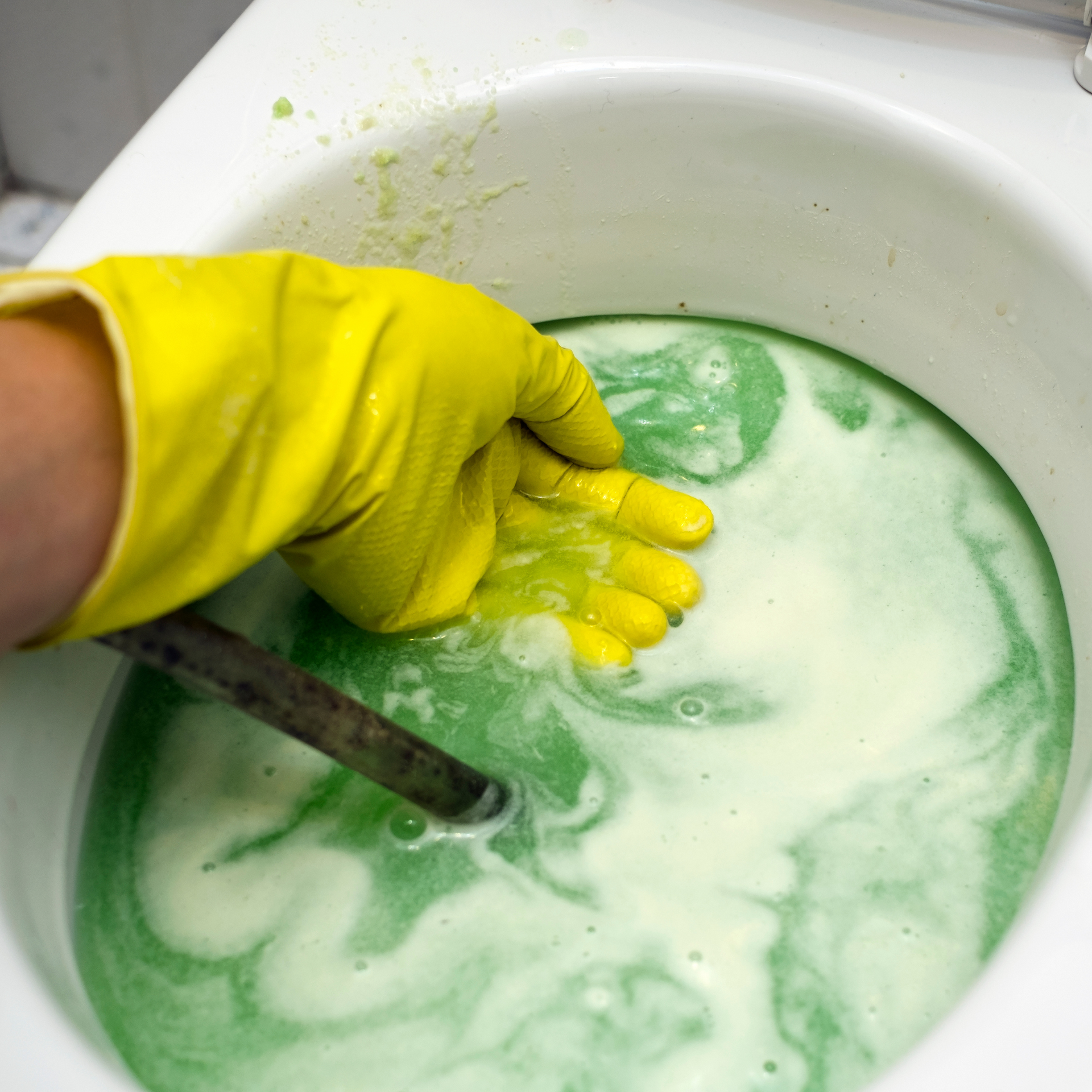 Ted & Bros Plumbing | person wearing a yellow glove is holding a hose in a bowl of green liquid