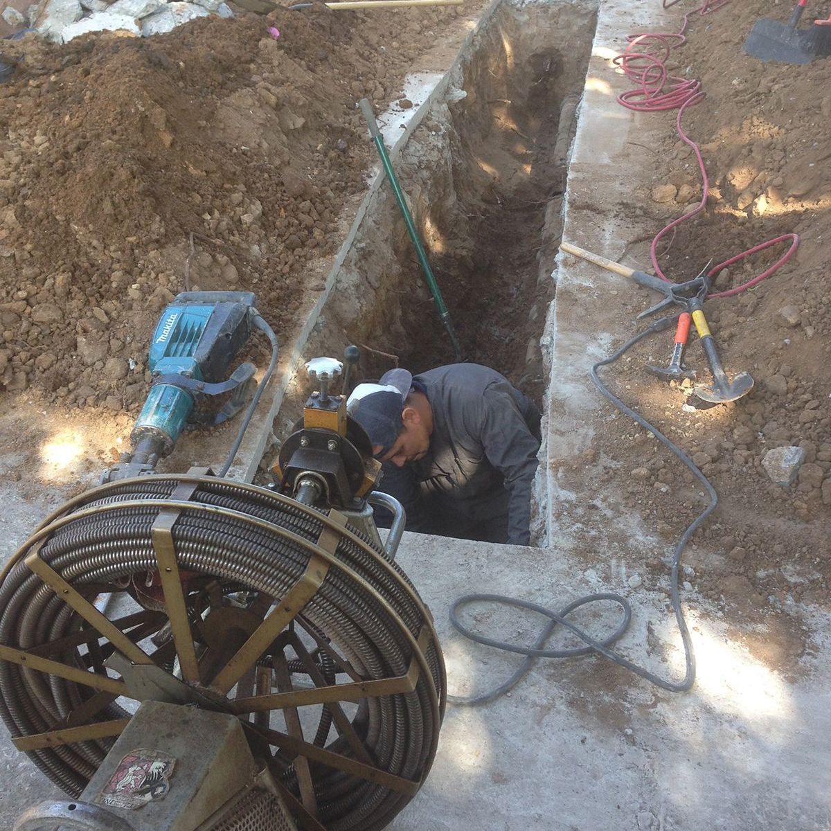 Ted & Bros Plumbing | man is working in a hole next to a hose reel