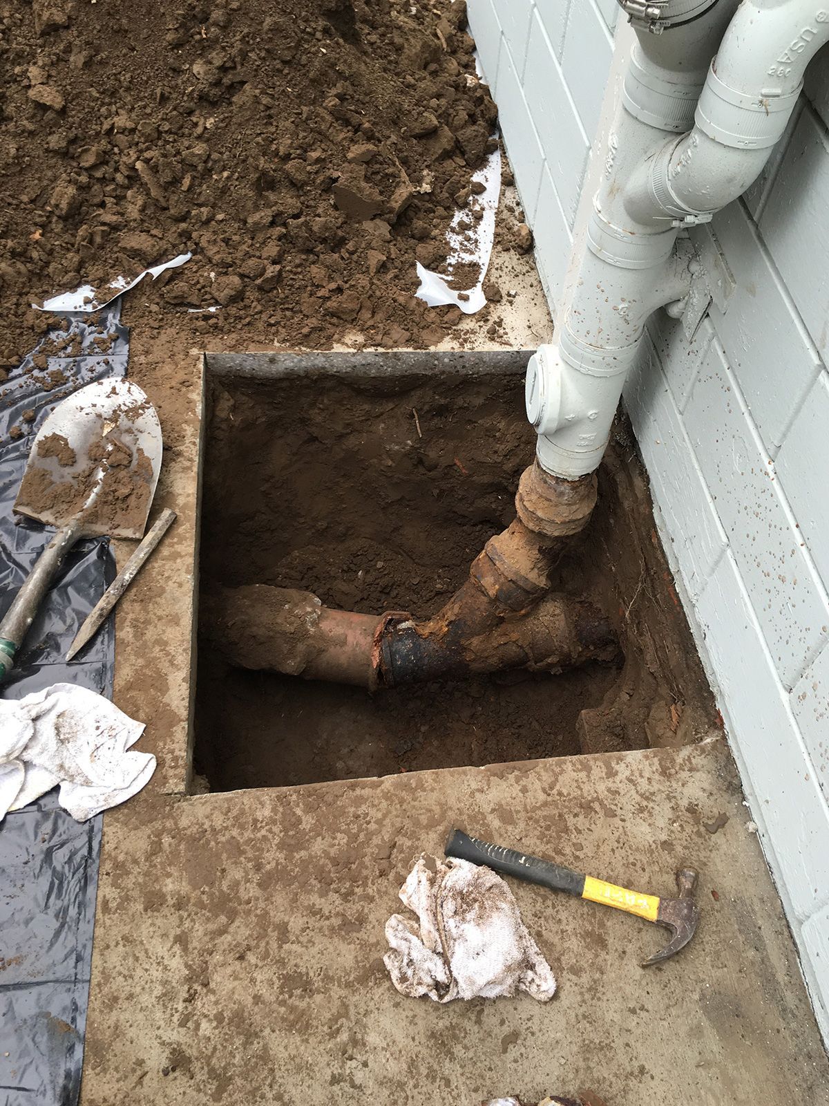 Ted & Bros Plumbing | pipe is being installed in a hole in the ground next to a wall.