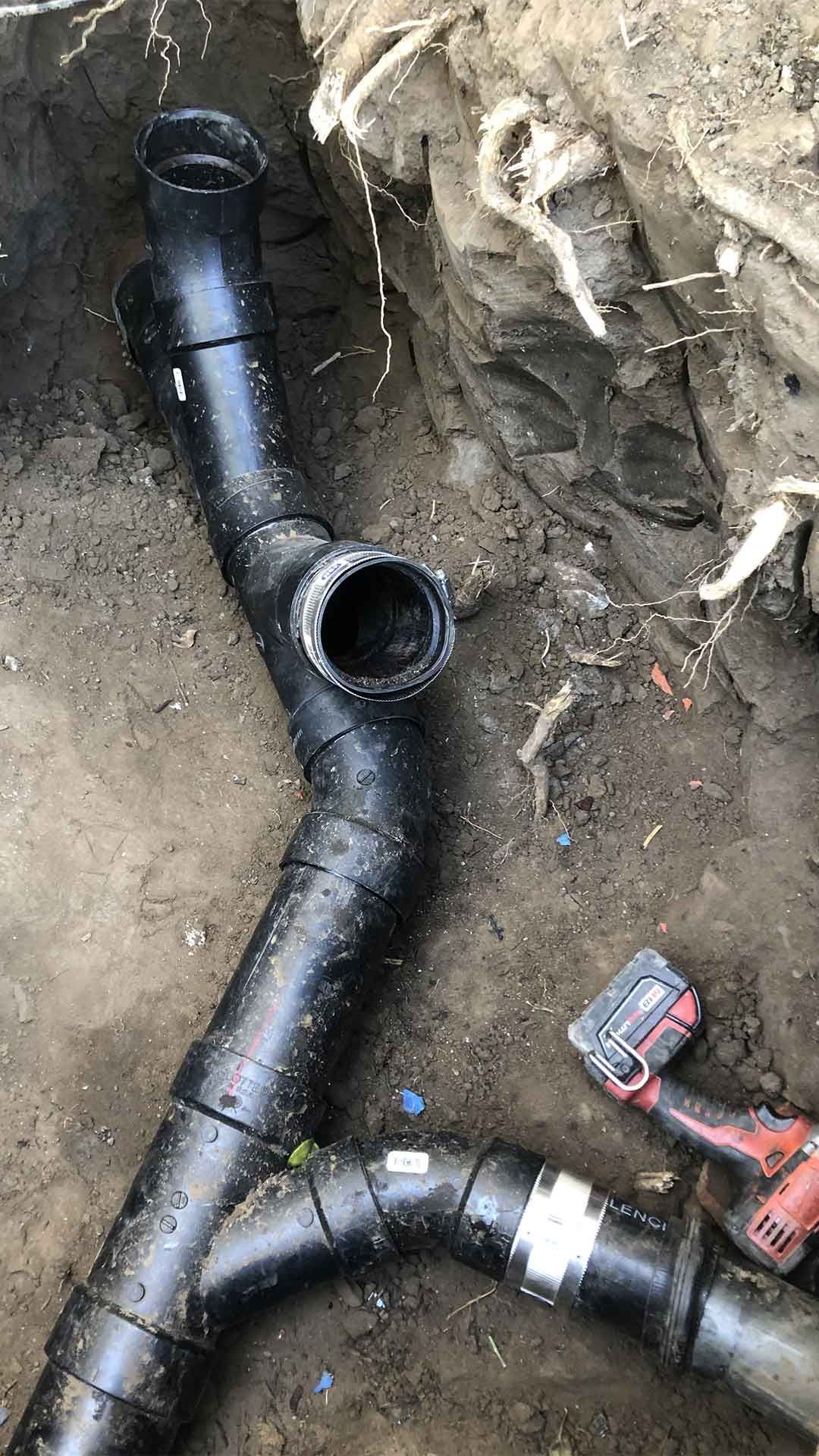 Ted & Bros Plumbing | bunch of black pipes are laying on the ground next to a drill.