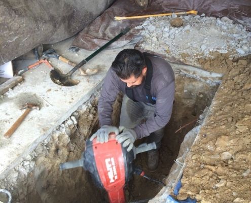 Ted & Bros Plumbing | man is using a Hilti hammer to dig a hole