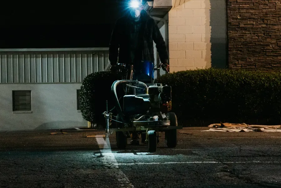 A man is using a machine to paint a white line on the road.