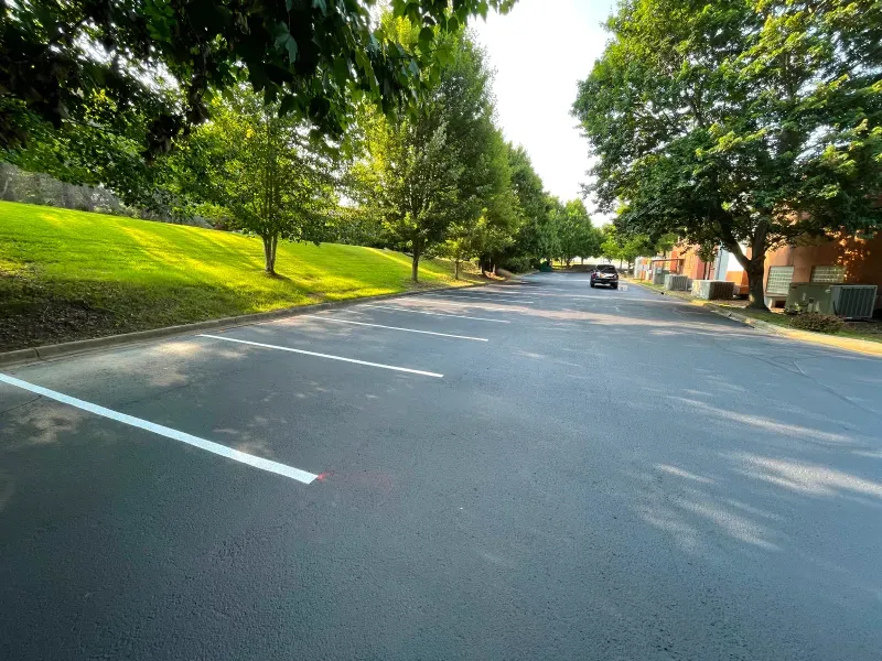A car is driving down a street next to a parking lot.