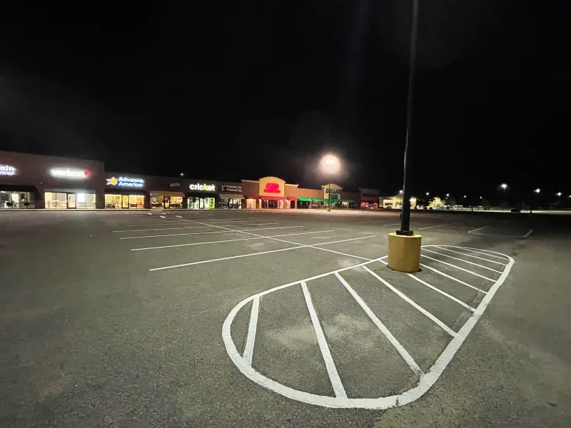 An empty parking lot at night with a handicapped parking space in the middle.