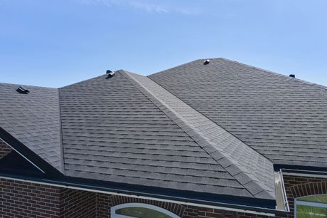 Close-up of a gray shingle roof with intersecting ridgelines under a blue sky