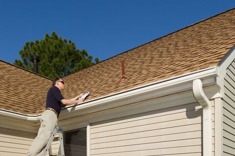 Man standing on a ladder painting white trim on a house roofline
