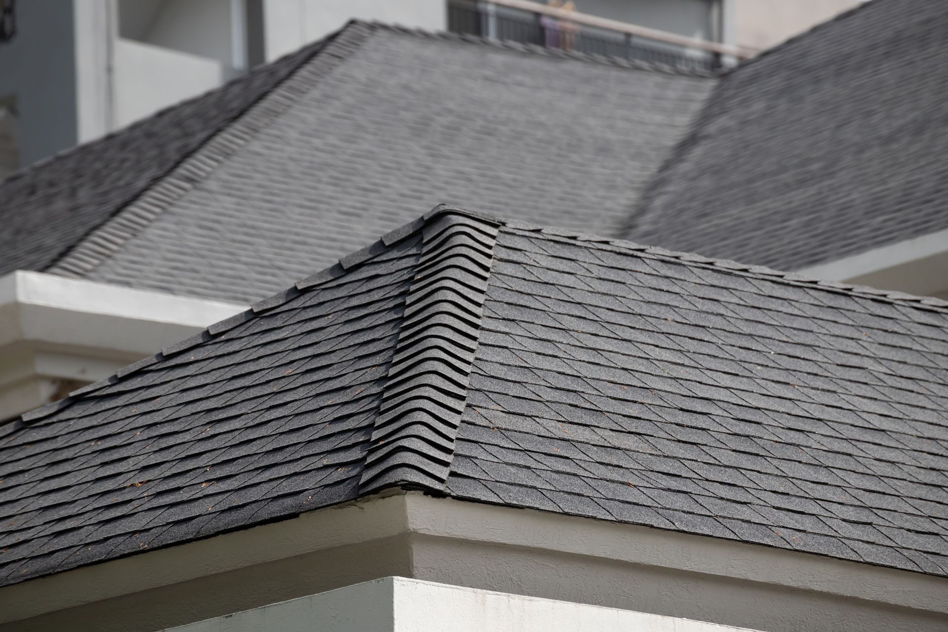 Close-up of a gray shingled roof with a dormer against a blurred building background