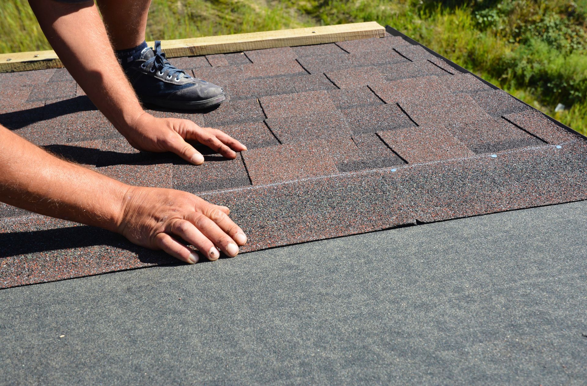 Hands aligning dark gray roof shingles on a rooftop edge