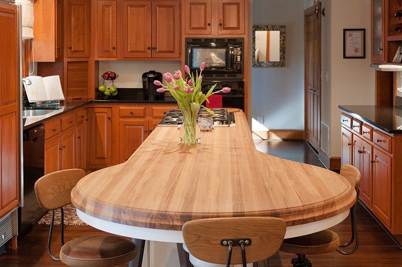 Warm white wooden kitchen with a long white oak island, stools, cabinets, and flowers in a vase.