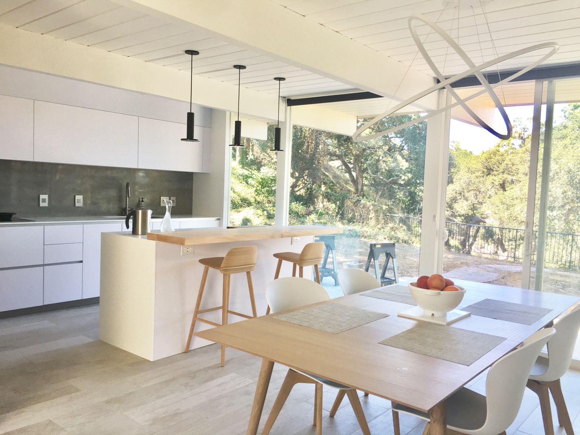 Modern open-plan kitchen and dining area with hard maple wood bar top, wood table, stools, and large windows overlooking greenery