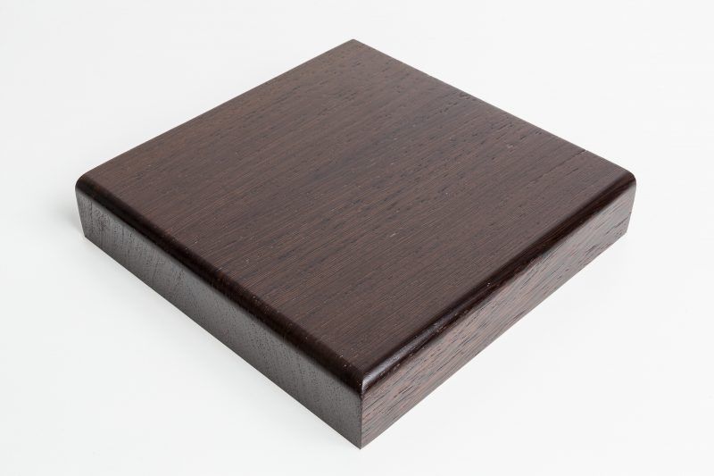 A square piece of wood is sitting on a white surface.