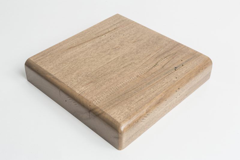 A square piece of wood is sitting on a white surface.