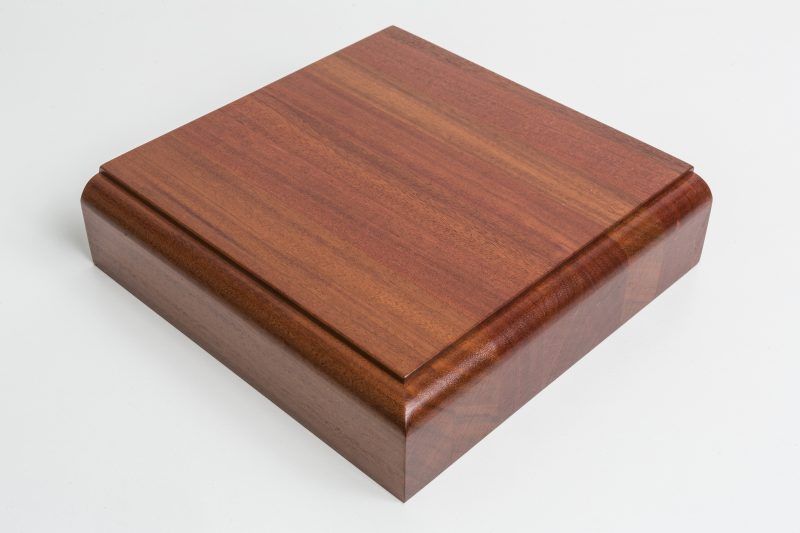 A square piece of wood is sitting on a white surface.