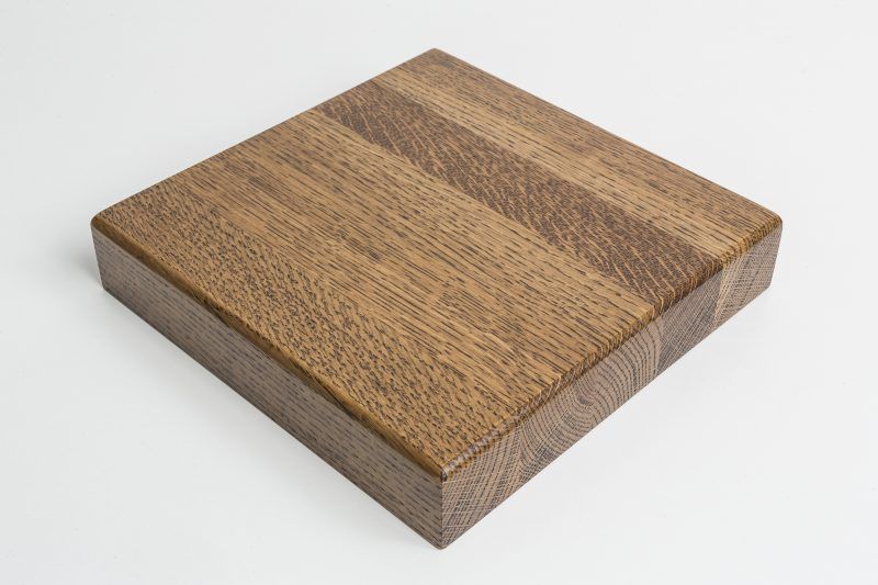 A square piece of wood is sitting on a white surface.