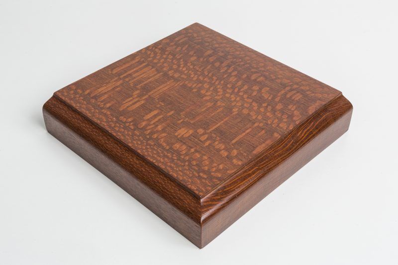 A square piece of wood is sitting on a white surface.