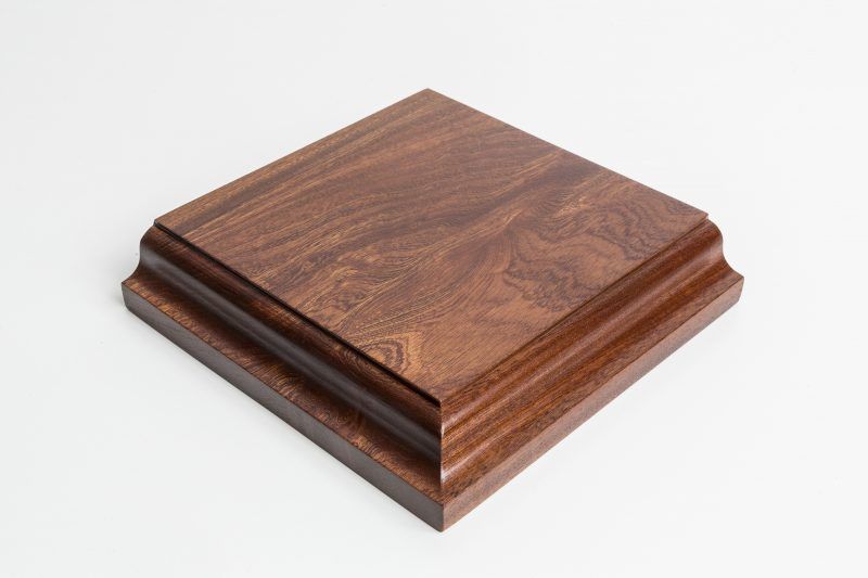 A square piece of wood is sitting on a white surface.