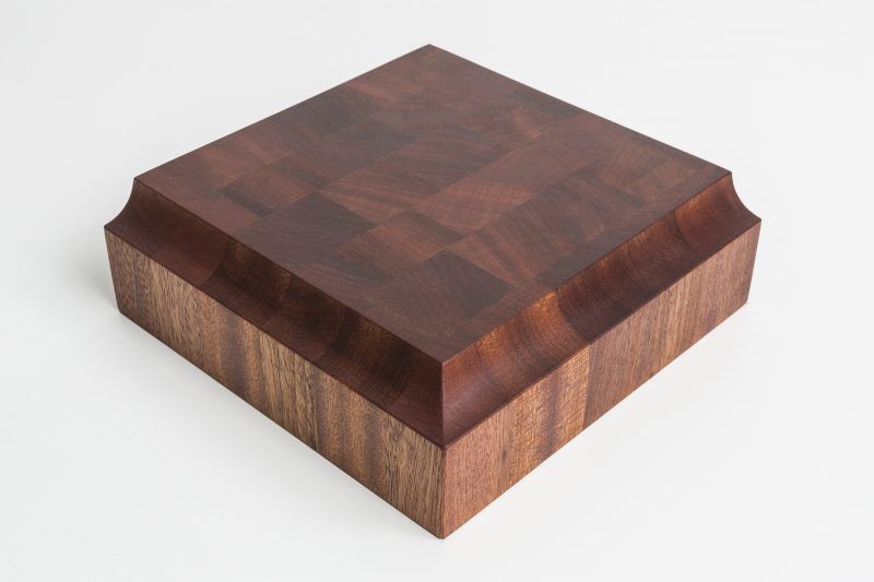 A square piece of wood is sitting on a white surface.