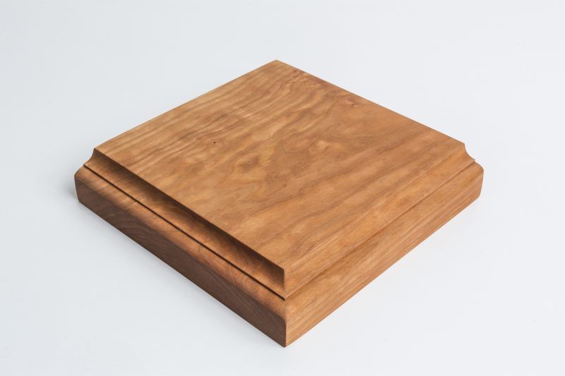 A square piece of wood is sitting on a white surface.