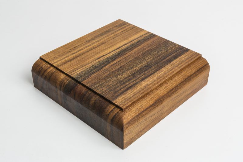 A square piece of wood is sitting on a white surface.