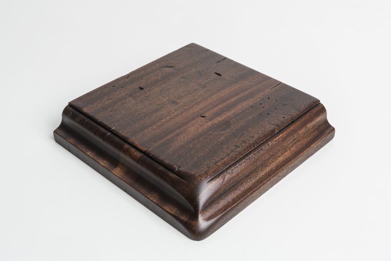 A square piece of wood is sitting on a white surface.