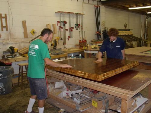 Two men are working on a wooden table in a workshop