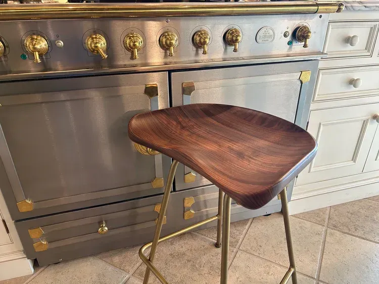 A wooden bar stool is sitting in front of a stove in a kitchen.