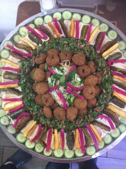 Falafel platter with cucumbers, pickles, and pickled vegetables arranged on a round metal tray.