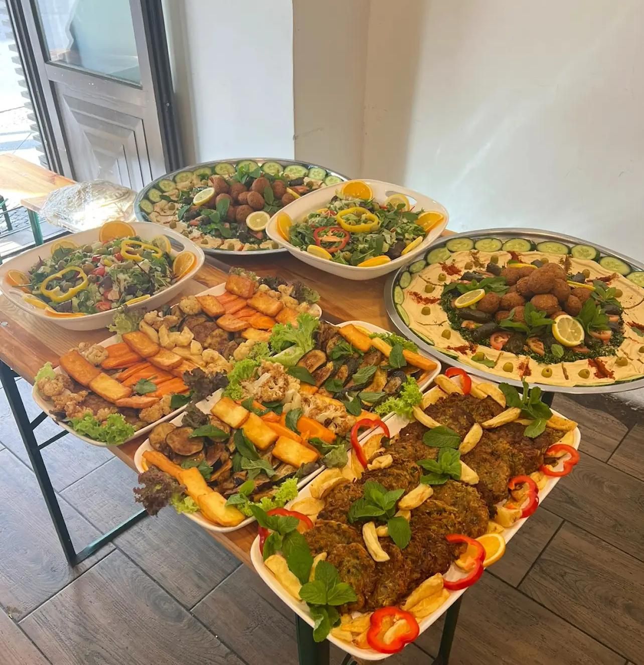 A table displays multiple platters of colorful Middle Eastern dishes, including falafel and salads.
