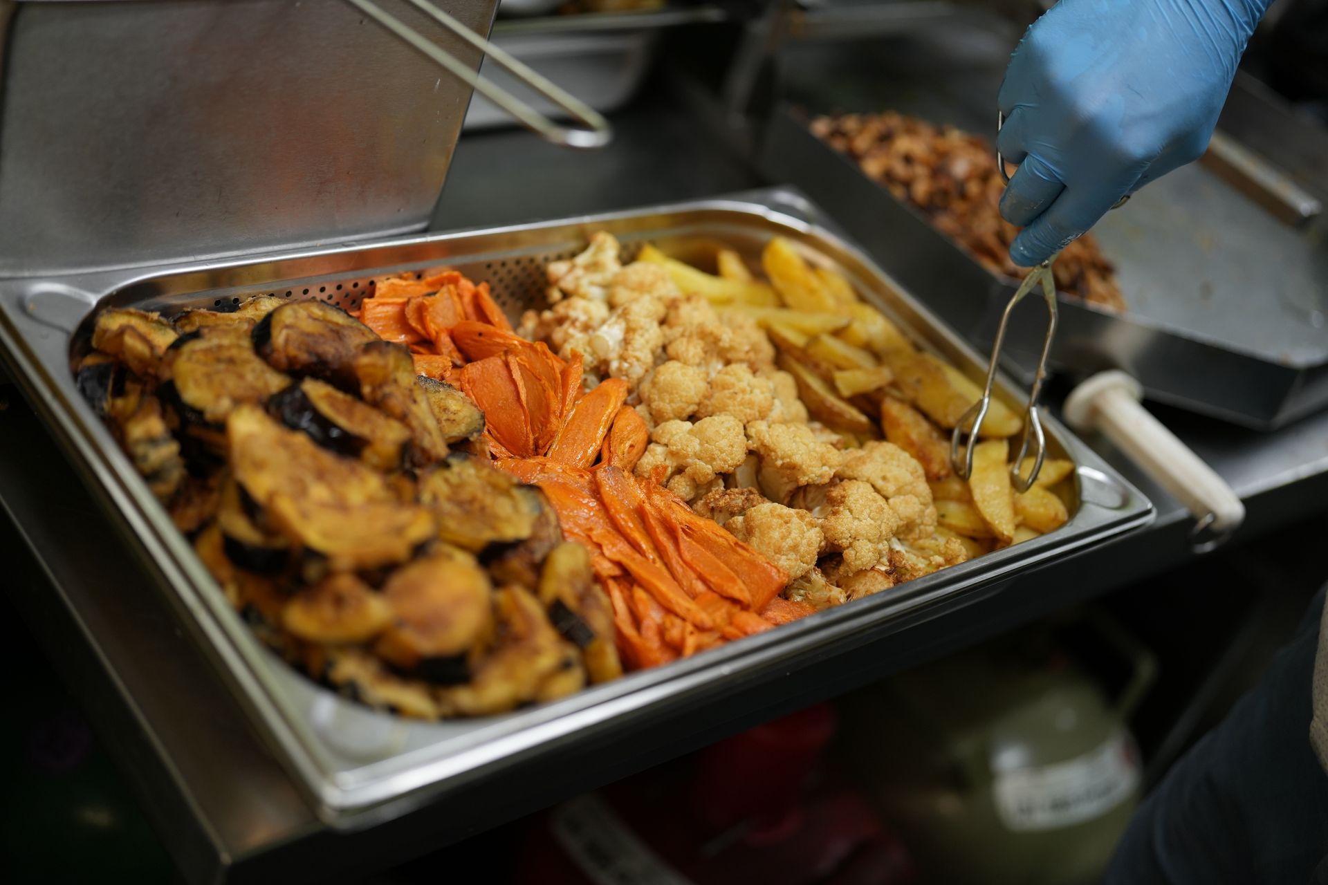 Tray with assorted fried vegetables, a hand with tongs serving food.