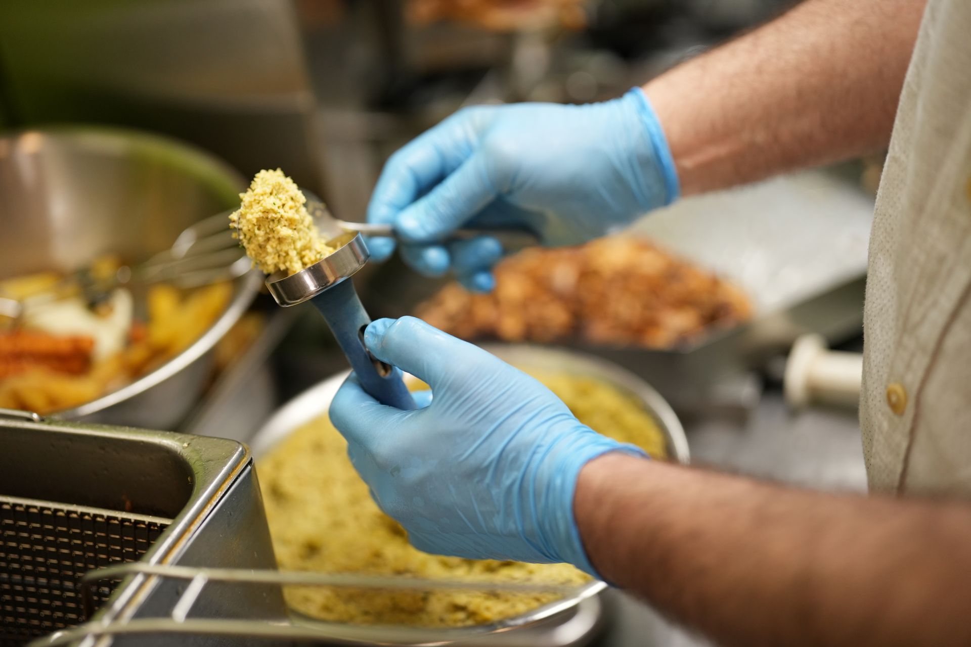 Chef wearing blue gloves shaping food in a kitchen.