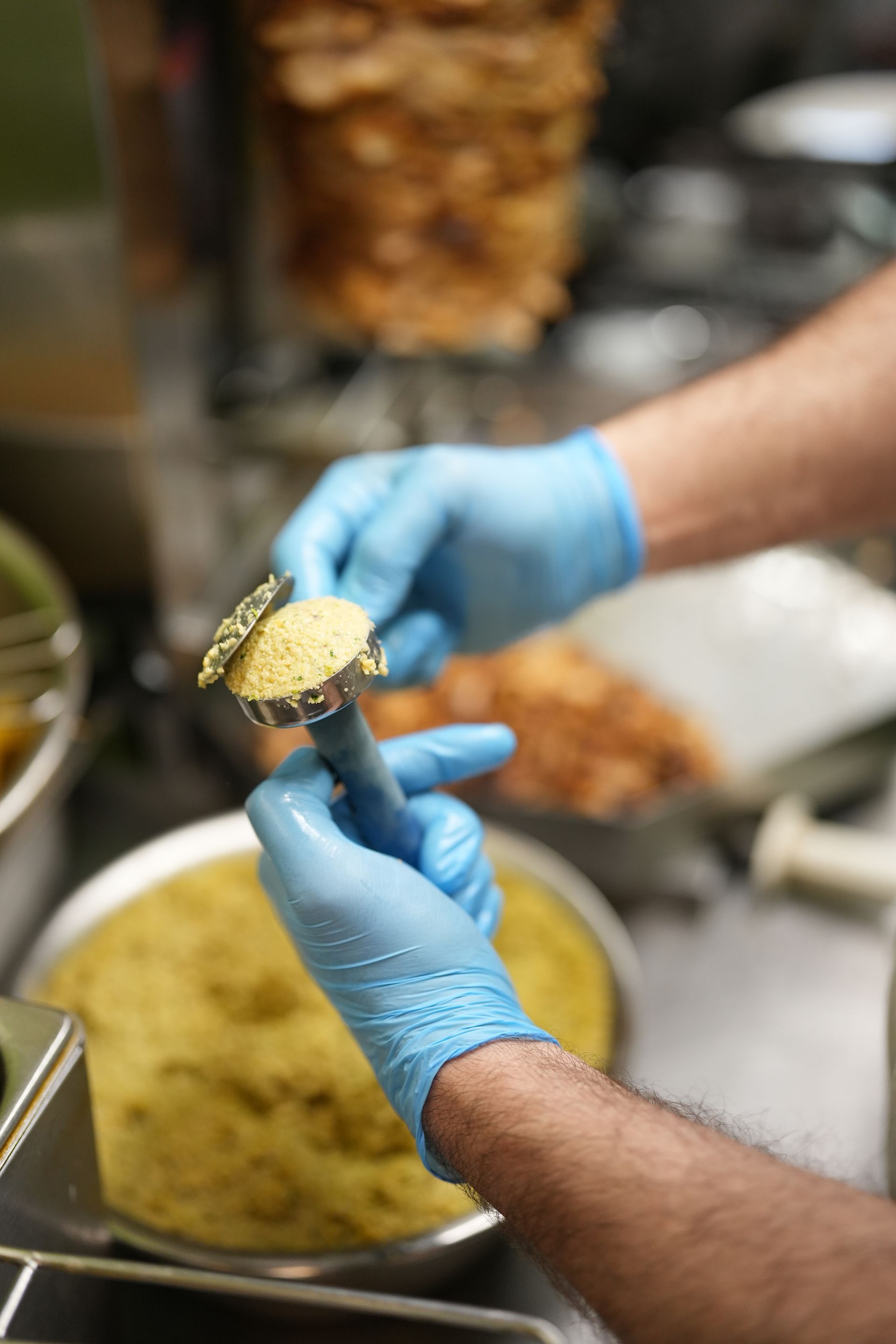 Hands in blue gloves forming falafel with a scoop, food preparation.