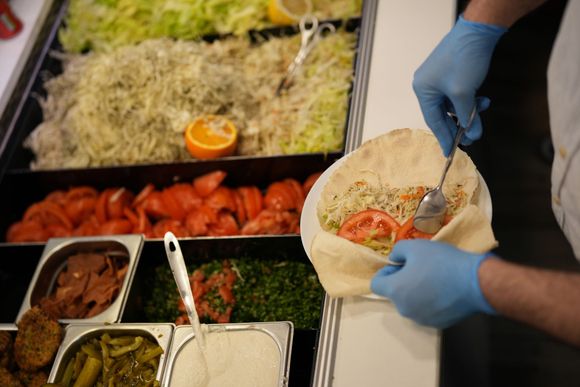 Person in blue gloves preparing a wrap with various ingredients at a food counter.