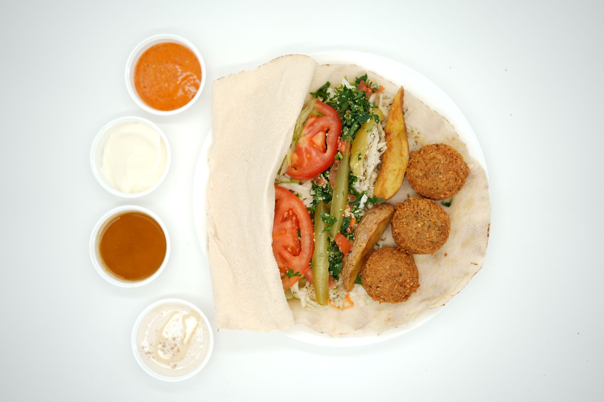 Falafel wrap with tomatoes, cucumber, and sauces in small bowls.