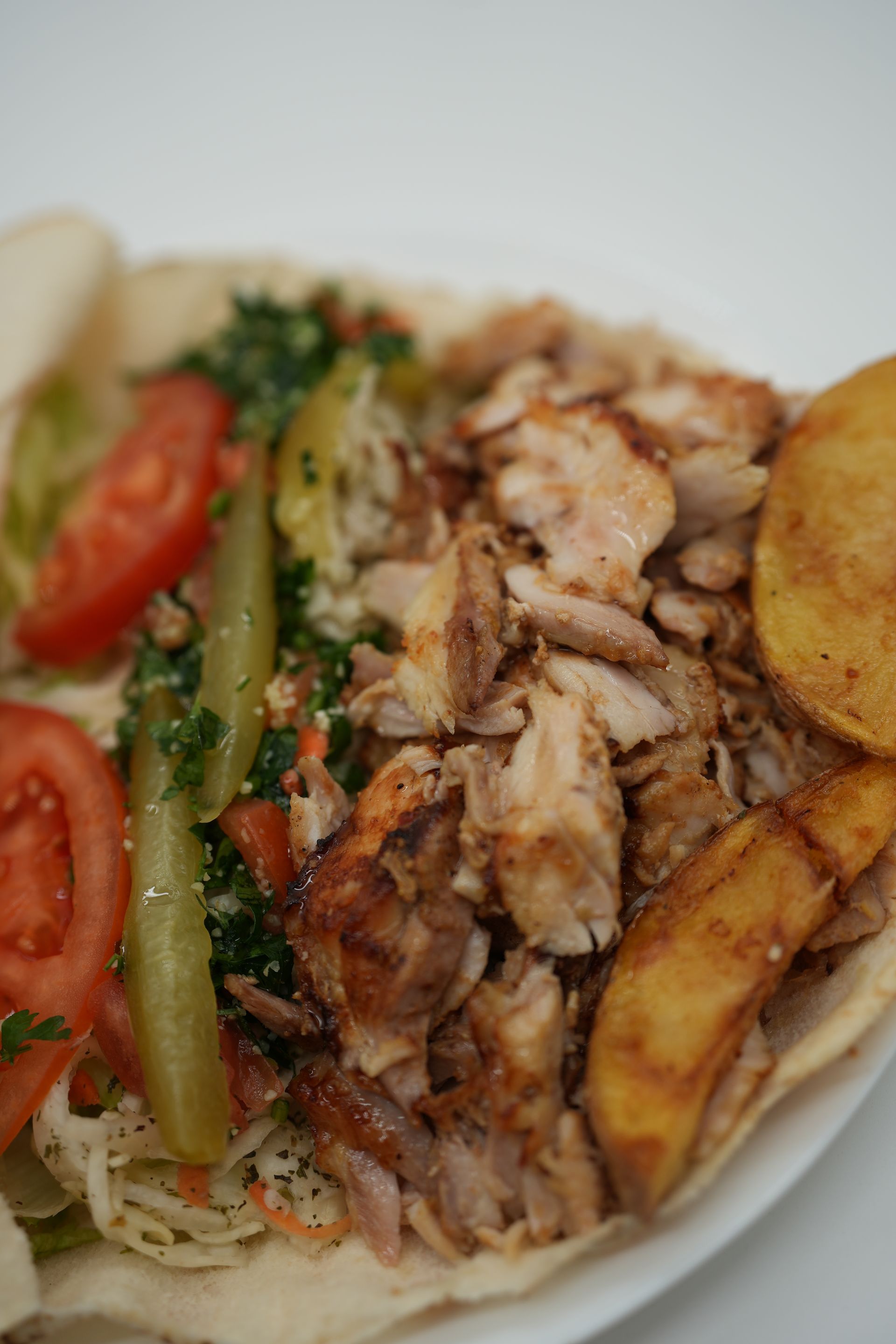 Shawarma wrap filled with chicken, tomatoes, pickles, lettuce, and fries.