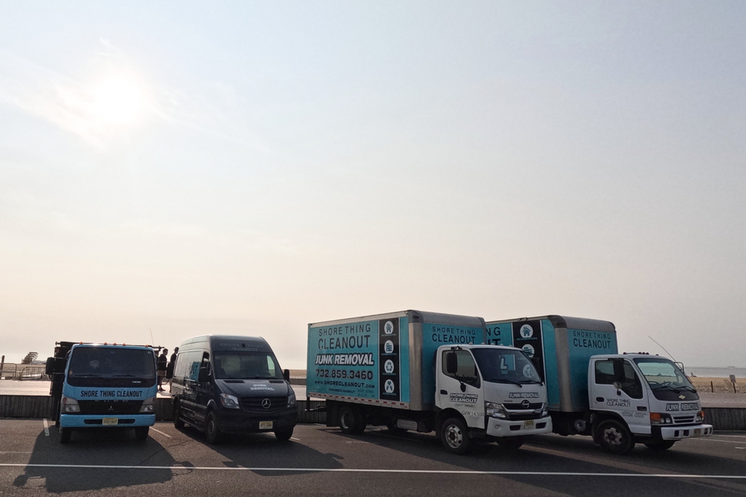 Trucks parked along a coastal road under a bright sky. One truck has a logo that reads