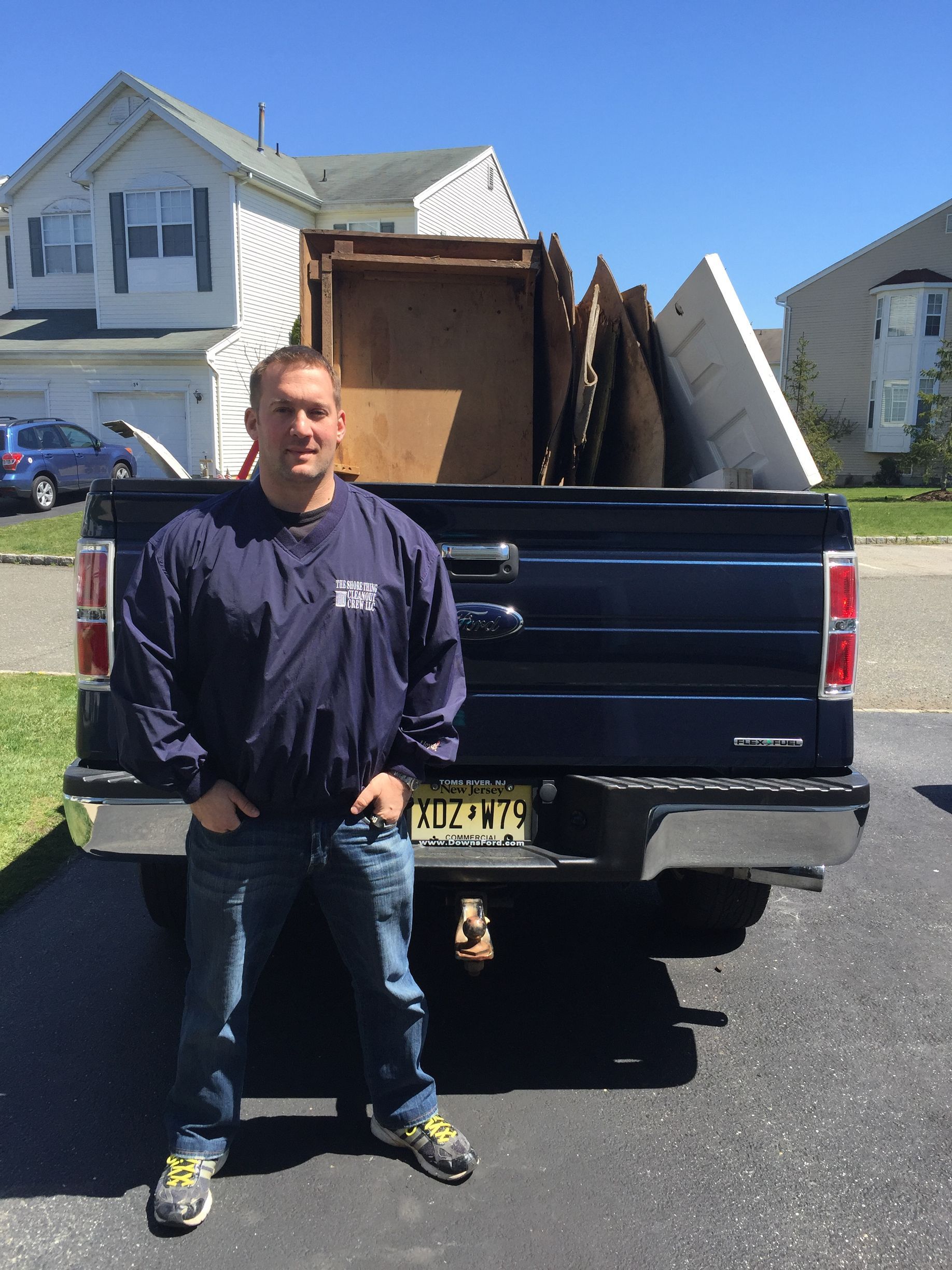 A man in blue overalls is standing in an office with his arms crossed