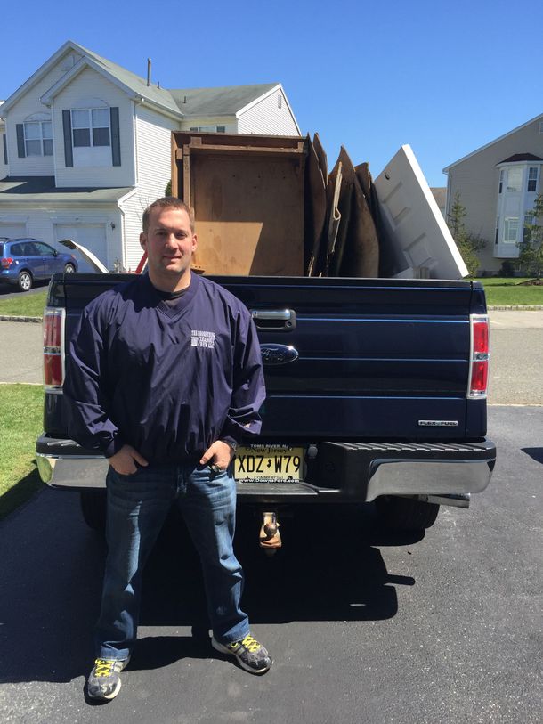 A man in blue overalls is standing in an office with his arms crossed